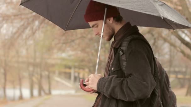 Genç adam bir telefon ve bir şemsiye yağmur altında — Stok video