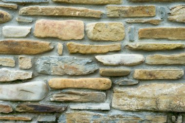 Arka planda çimento eklemleri olan farklı boyutlarda taşlar duvara monte edilmiş.