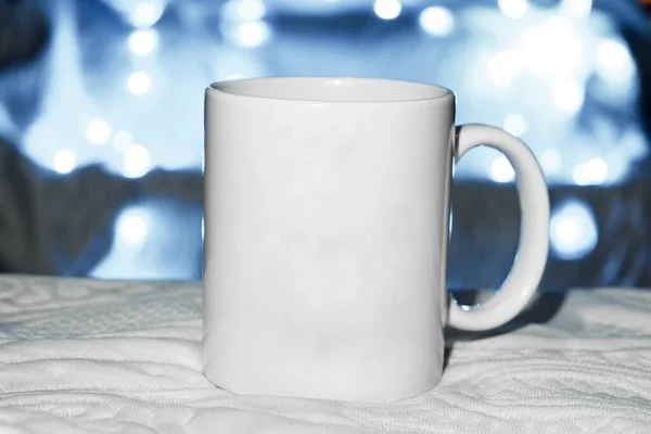 ベッドの上の白いマグカップ白い布のマグカップ広告用のスペース青い背景 焦点を絞ったライトの背景 広告コンセプト — ストック写真