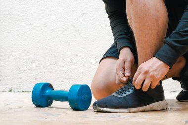 Eğitime başlamadan önce ayakkabılarını dambıl ve şişenin yanına mavi suyla bağlayan bir adam. Evde egzersiz, beyaz arka plan. Fitness konsepti. sağlık kavramı, reklam metni için alan