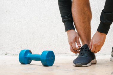 Egzersiz yapmadan önce ayakkabısını mavi halterin yanında bağlayan bir adam. Evde egzersiz, beyaz arka plan. Fitness konsepti. sağlık kavramı, reklam metni için alan