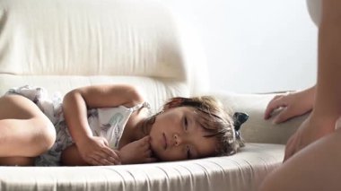 Genç bir Latin anne, küçük kızını öpüyor ve okşuyor. Kanepede uyuyor. Evde hassas bir aile anı..