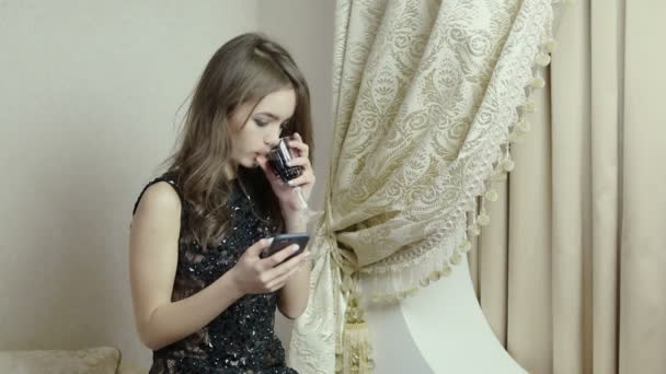 Uma jovem bonita a beber vinho tinto na sala de estar, a ler uma mensagem do teu telemóvel — Vídeo de Stock