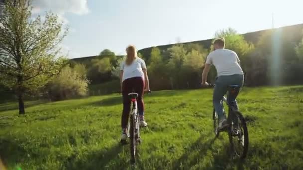 Reeks 5 video: paar fietsen rijden op de groene weide bij zonsondergang. — Stockvideo
