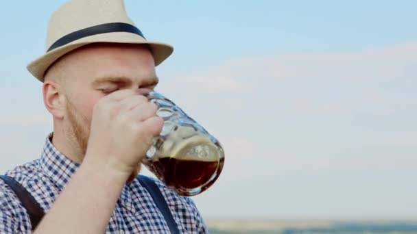 Man with leather suspenders outdoors drinking beer. — Stock Video