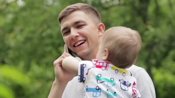 Papá joven con su hijo en brazos hablando por teléfono — Vídeo de stock