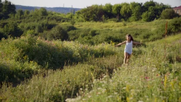 A menina corre em um caminho na natureza entre as flores silvestres . — Vídeo de Stock