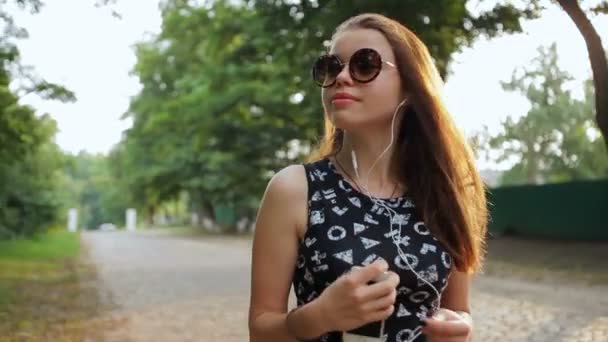 Chica atractiva caminando y escuchando música en los auriculares . — Vídeo de stock