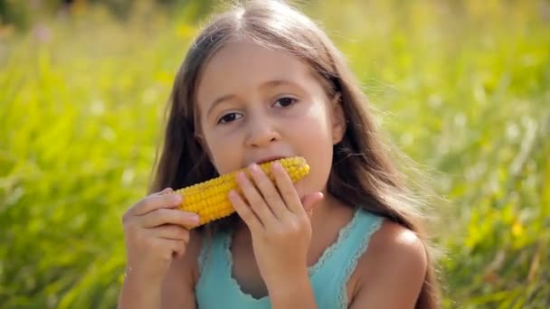 Meisje eten een gekookte maïs buitenshuis op een zonnige dag. — Stockvideo