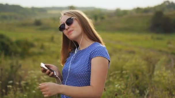 Jong meisje in zonnebril luisteren naar muziek met koptelefoon buitenshuis. — Stockvideo