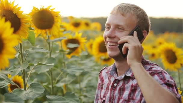 Gelukkig jonge boer spreekt op de telefoon in een veld met zonnebloemen. — Stockvideo