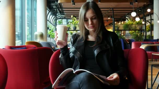 Kaunis nainen lukee lehteä odottaessaan modernissa kahvilassa — kuvapankkivideo
