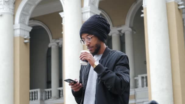 Portret van gemengde ras man, staande op de straat drinken koffie en gebruik smartphone — Stockvideo