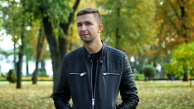 Sonbahar parkında siyah deri ceketli bir adamın resmi. Kameraya bakıyor.