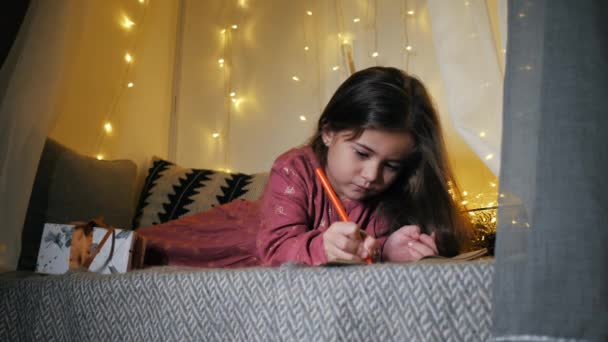 Süßes Kind schreibt einen Brief an den Weihnachtsmann auf der Fensterbank, dekoriert für Weihnachten, Vorbereitung auf Urlaub, Feiertage und Feiern — Stockvideo