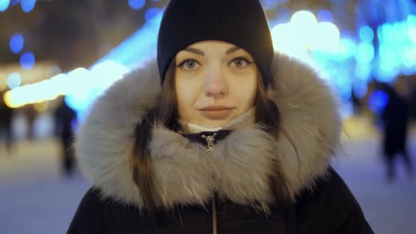 Noel ve yeni yılı kutlamak için süslenmiş bir sokakta çelenk ışıklarıyla duran güzel genç bir kadın.. — Stok video