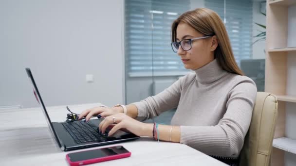 Aranyos nő, szemüveges laptopnál dolgozik, szöveget ír az irodában, dolgozik a számítógépen.. — Stock videók
