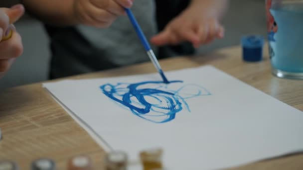Großaufnahme der Hände eines kleinen Kindes zeichnet mit Pinsel und blauer Farbe auf einem Blatt Papier zu Hause — Stockvideo