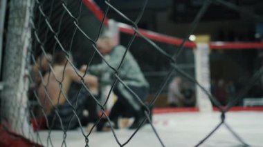 Sekizgen raundunun arasında bulanık dövüşçü, su içiyor, koç tavsiye veriyor, bir kafeste karma dövüş sanatları turnuvası.