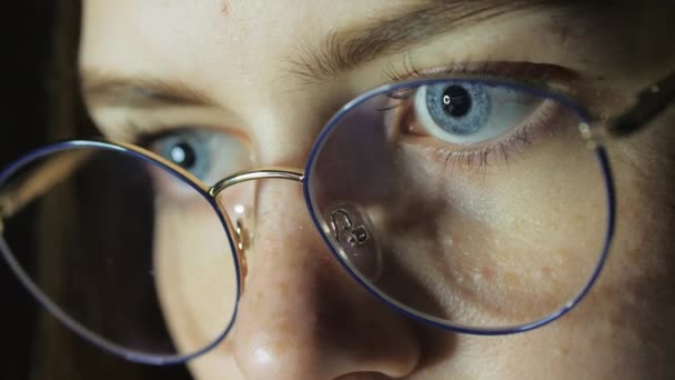 Крупным планом глаза девочки-подростка в очках смотрят на монитор, играют в игру, читают, учатся — стоковое видео