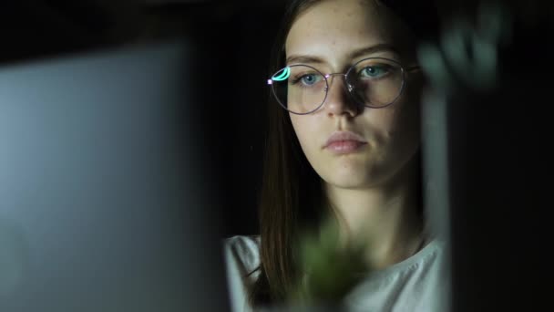 Nastolatka w okularach patrzy na monitor, gra w grę, czyta, uczy się późno w nocy — Wideo stockowe