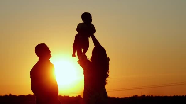 Nierozpoznawalna sylwetka rodziny o zachodzie słońca, mama rzuca dziecko, wartości rodzinne — Wideo stockowe