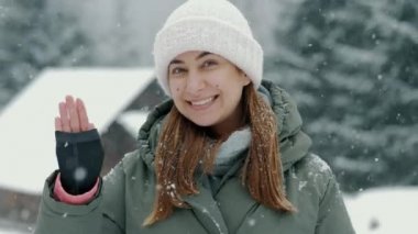 Mutlu bir kadının portresi. Kış ormanındaki kar yağışı sırasında selam verip kameraya hava öpücüğü yolluyor.