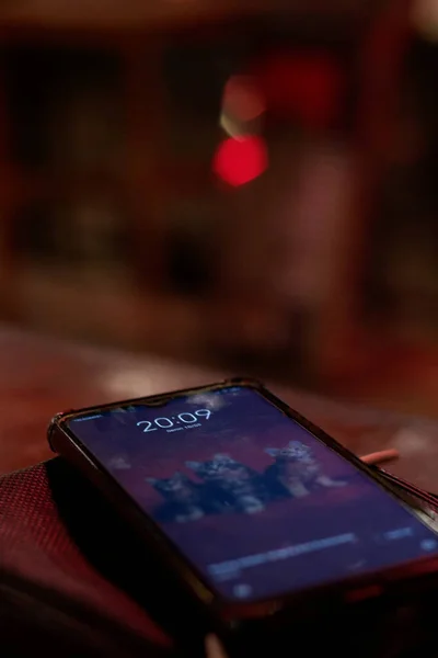 A cat wallpaper on a smartphone that is placed on a table at night in a coffee shop.