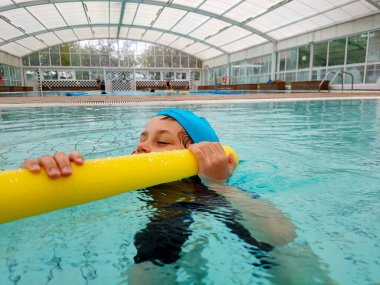 Havuzdaki çocuk yüzmeyi öğreniyor.