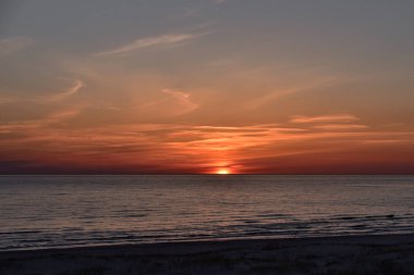 Gün batımı sakin bir su yüzeyi ve güneş ışınları tarafından yaratılmış güzel bir gökyüzü ufkun ötesine doğru yavaşça kayıyor.