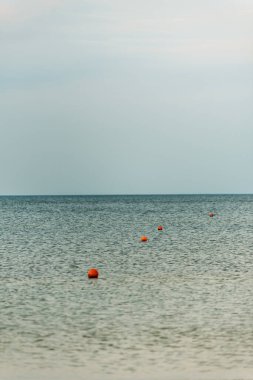 Turuncu şamandıraların yuvarlak şekillerle yüzdüğü sakin su yüzeyinde biniciler ve denizciler için güvenli bölge işaretleri var.