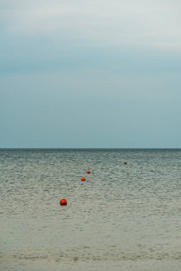 Turuncu şamandıraların yuvarlak şekillerle yüzdüğü sakin su yüzeyinde biniciler ve denizciler için güvenli bölge işaretleri var.