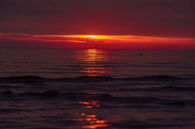 Güneş yavaşça su ufkunun kenarına yaklaşıyor, bulutların arasında saklanıyor ve suların sakin yüzeyinde turuncu bir güneş yolu bırakıyor.