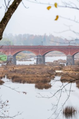 Sonbaharda eski bir tuğla köprü ve köprünün altından daha geniş sulara akan bir nehir.