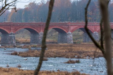 Sonbaharda eski bir tuğla köprü ve köprünün altından daha geniş sulara akan bir nehir.