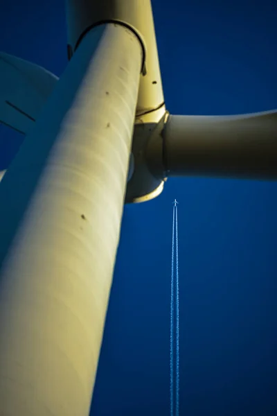 wind generator, blue sky and airplane high in the air fly to its destination in clear daylight and leave a white stripe behind