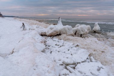 Antik tekne kışın buzla kaplanmış olarak rıhtımda ve deniz suyu ahşap yığınları yıkıyor.