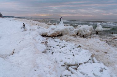 Antik tekne kışın buzla kaplanmış olarak rıhtımda ve deniz suyu ahşap yığınları yıkıyor.
