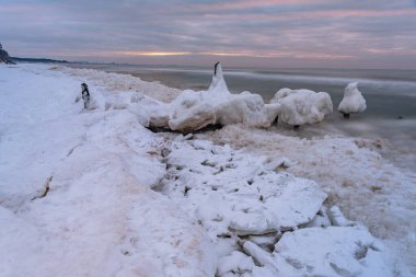 Antik tekne kışın buzla kaplanmış olarak rıhtımda ve deniz suyu ahşap yığınları yıkıyor.