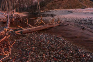 Deniz kıyısında gün batımı ve gün batımının renkli renkleriyle nehrin kaynağı ve güneşi gizleyen bulutlu güzel bir gökyüzü.