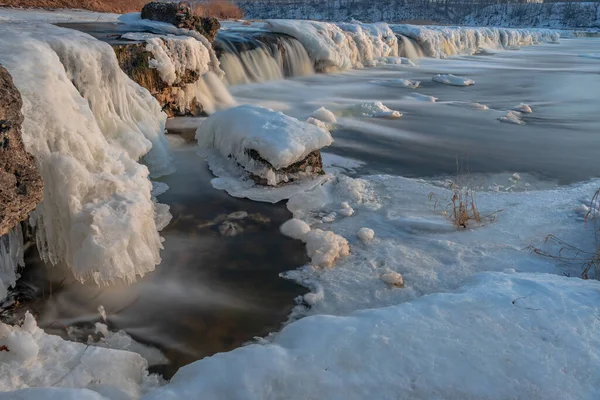 a wide waterfall in the winter with ice and snow merged in a long exposure creating a relaxing feeling watching the water flow