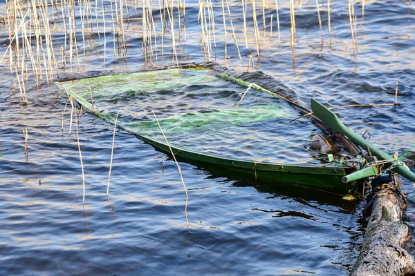a green rowing boat sinking into the water on a sunny spring day, walking along the shore of a lake