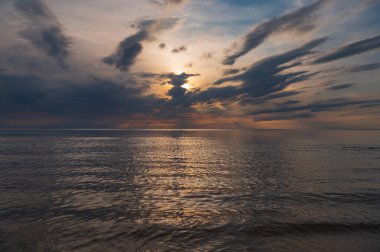 sunset in the sea with clouds and calm water on the surface of which sunlight reflects by creating a light path