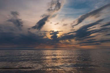 sunset in the sea with clouds and calm water on the surface of which sunlight reflects by creating a light path