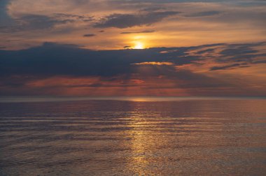 sunset in the sea with clouds and calm water on the surface of which sunlight reflects by creating a light path