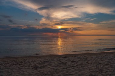 sunset in the sea with clouds and calm water on the surface of which sunlight reflects by creating a light path