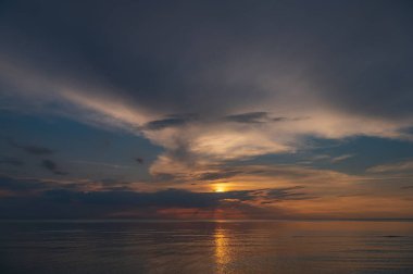sunset in the sea with clouds and calm water on the surface of which sunlight reflects by creating a light path