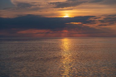 sunset in the sea with clouds and calm water on the surface of which sunlight reflects by creating a light path