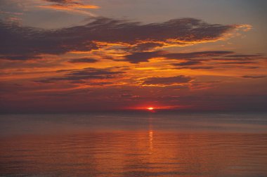 sunset in the sea with clouds and calm water on the surface of which sunlight reflects by creating a light path