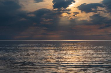 sunset in the sea with clouds and calm water on the surface of which sunlight reflects by creating a light path